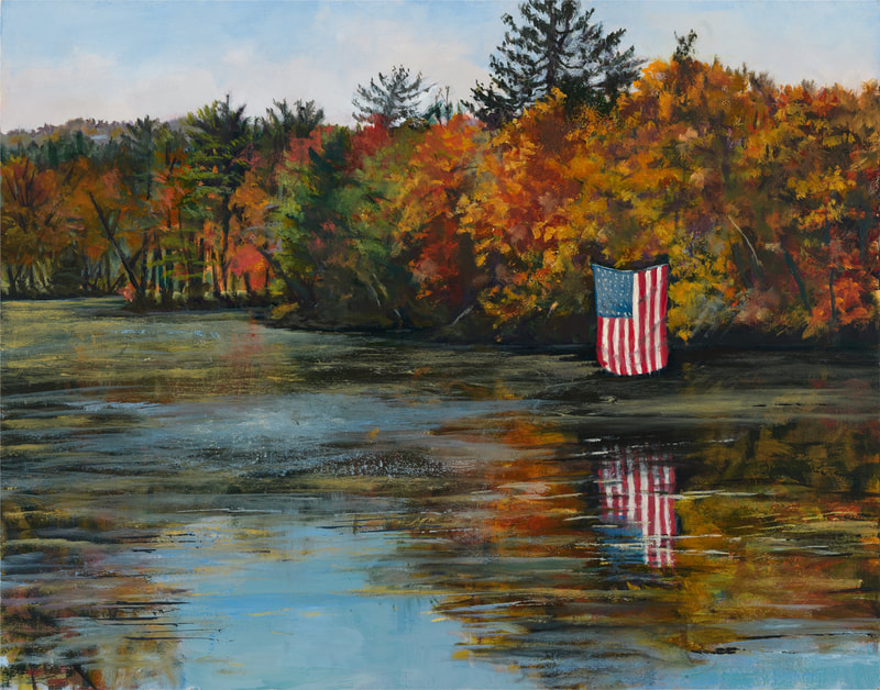 An American flag hangs over a pond. The flag and colorful autumnal trees in the background are reflected in the pond's water. 